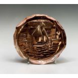 A Newlyn copper small circular tray, repousse decorated with a sailboat entering a harbour,