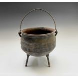 A cast iron cauldron with handle, raised on three legs. Overall height 42cm.