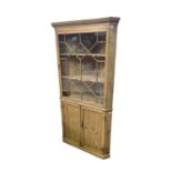 A 19th century pine standing corner cupboard, with an astragal glazed door enclosing three