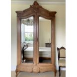 A French walnut armoire, late 19th century, with carved decoration, the two mirror doors enclosing a