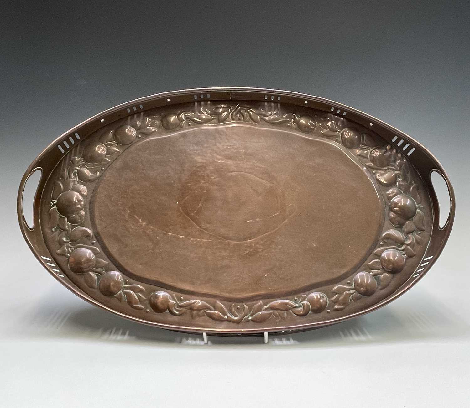 A Newlyn copper oval tray, circa 1910, the raised edge with twin handles, the border repousse