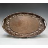 A Newlyn copper oval tray, circa 1910, the raised edge with twin handles, the border repousse