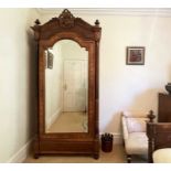 A French rosewood wardrobe, late 19th century, with arched and carved top, the mirrored door