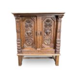 A Continental oak side cabinet, late 19th century, the two doors carved with cherub masks, fruit