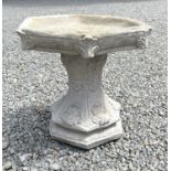 A composition stone birdbath, the hexagonal top raised on a base with acanthus leaf decoration.