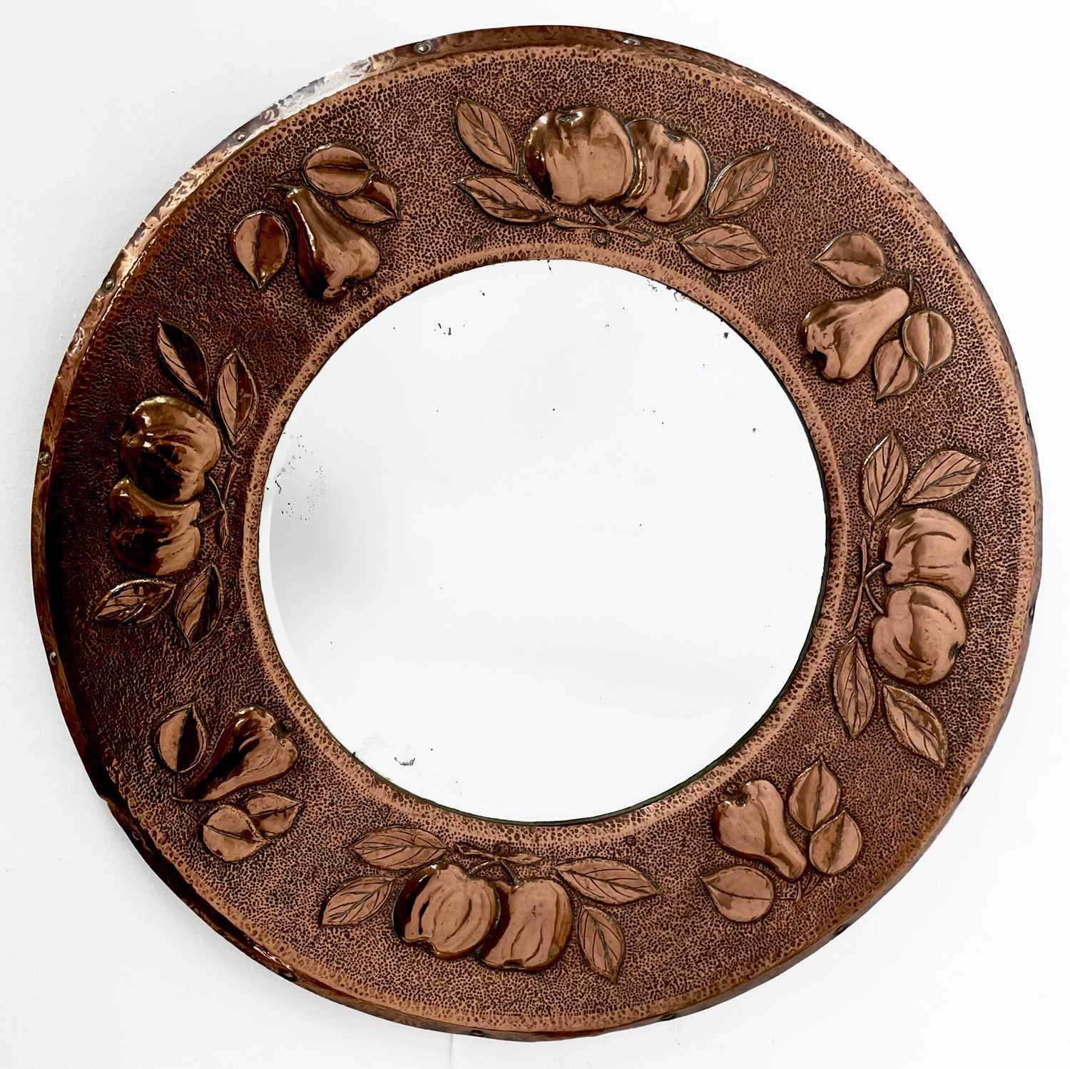 An early Newlyn copper circular wall mirror, circa 1900, repousse decorated with pears and medlars
