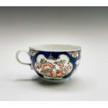 A Worcester porcelain teacup and saucer, circa 1770, the blue scale ground decorated with panels