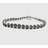 A diamond line bracelet set in white metal with 22 heart shaped links each with a trefoil of