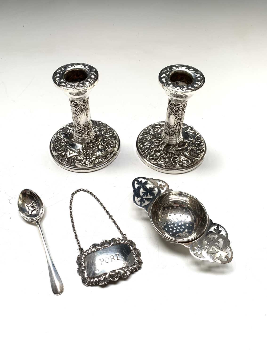 A pair of low embossed filled silver candlesticks, a silver tea strainer, a silver port label and