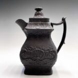 A black basalt hot water jug and cover, circa 1800, with dolphin and shell moulded decoration,