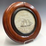 A sailors woolwork circular panel of a three masted sailing ship on water, within a mahogany and