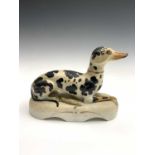 A Staffordshire figure of a recumbent black and white greyhound, 19th century, painted with Disraeli