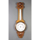 A late Victorian aneroid barometer and thermometer with porcelain dial, contained in a carved oak