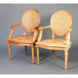 A pair of Empire style bleached hardwood open arm chairs with woven cane seats and backs, raised