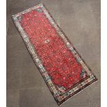 A red ground Persian rug with all over geometric design within a 3 row border 287cm x 104cm
