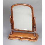 A Victorian arched plate dressing table mirror contained in a mahogany swing frame on a serpentine