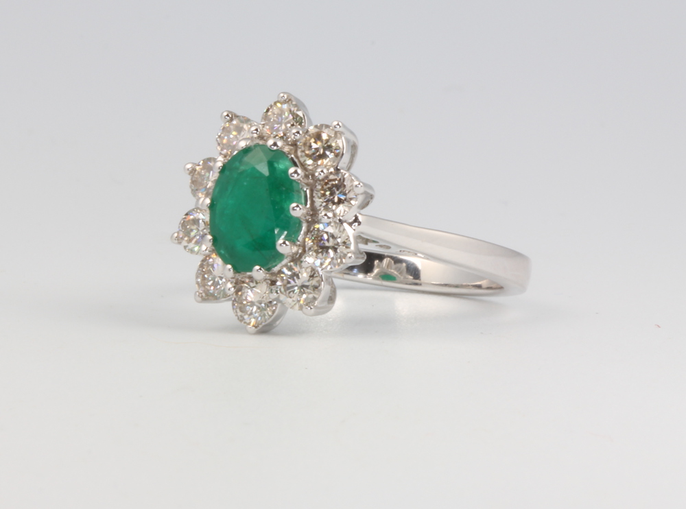 An 18ct white gold oval emerald and diamond cluster ring, the centre stone approx. 1.2ct, the