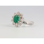 An 18ct white gold oval emerald and diamond cluster ring, the centre stone approx. 1.2ct, the