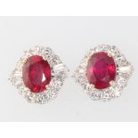 A pair of 18ct white gold oval ruby and diamond cluster earrings, the centre oval treated stones