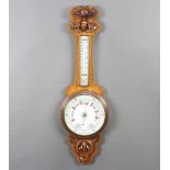 An Edwardian aneroid barometer and thermometer with porcelain dial, contained in a carved oak