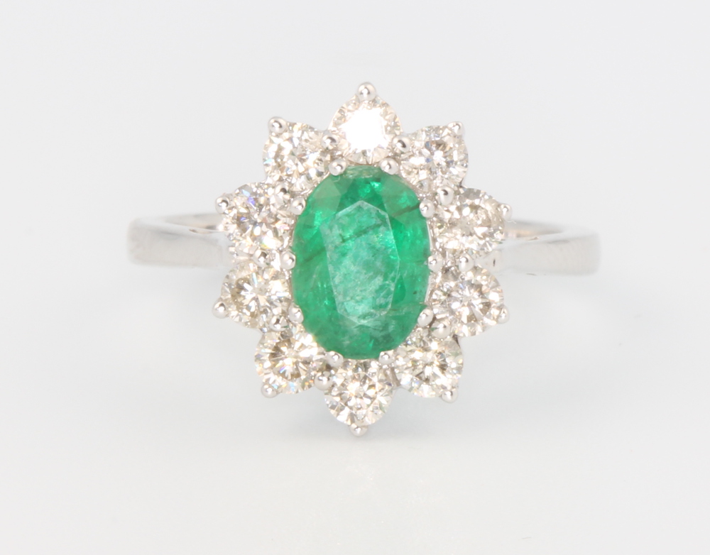 An 18ct white gold oval emerald and diamond ring, the centre cut stone 1.2ct surrounded by 10