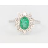 An 18ct white gold oval emerald and diamond ring, the centre cut stone 1.2ct surrounded by 10