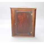 A Georgian mahogany hanging corner cabinet with moulded cornice, fitted shelves enclosed by a