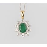 An 18ct oval white gold emerald and diamond cluster pendant, the centre emerald 1ct, the brilliant