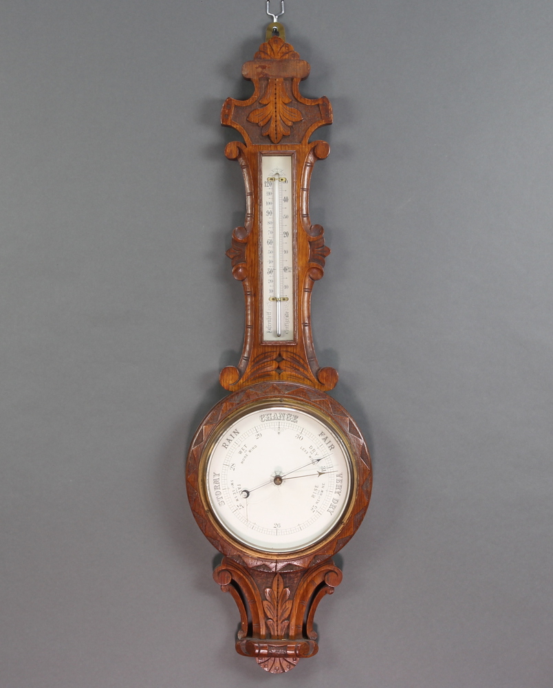 A Victorian aneroid barometer and thermometer contained in a carved oak wheel case 88cm x 26cm