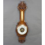An aneroid barometer and thermometer contained in a carved oak wheel case with porcelain dial 90cm h