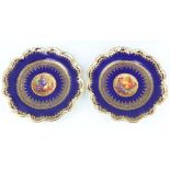 A pair of crescent china plates decorated with panels of fruit on a blue and gilt ground,