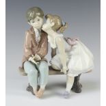 A Lladro group of a young couple sitting on a bench kissing 7635 19cm