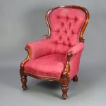 A Victorian carved mahogany show frame armchair upholstered in red buttoned material, raised on