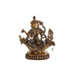 A TIBETAN GILT BRONZE FOUR ARM DEITY seated on a scaly mythical sea creature, inset with coral and