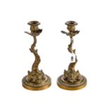 A PAIR OF 19TH CENTURY CAST BRASS DOLPHIN FORM CANDLESTICKS raised on circular leaf edge bases, each