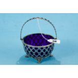 A GEORGE V CIRCULAR PIERCED SILVER SWING HANDLE SUGAR BASIN, blue glass liner, raised on scroll