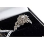A LADY'S WHITE METAL DIAMOND CLUSTER RING with bark finish shoulders, un-hallmarked, size P,