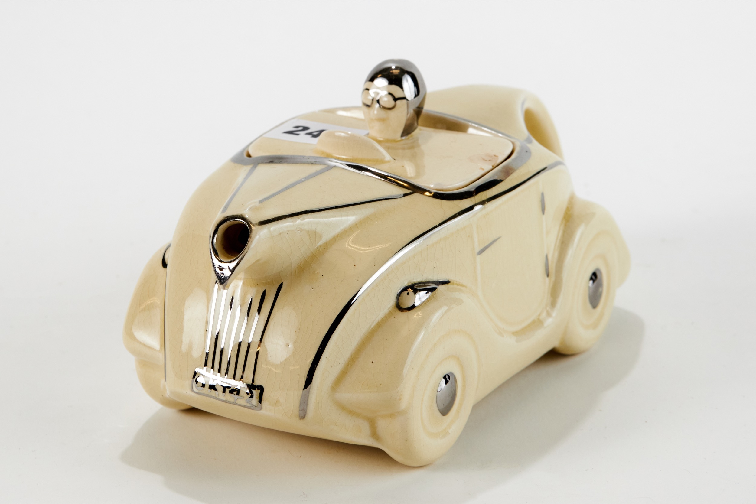 AN ART DECO CREAM GLAZED POTTERY RACING CAR TEAPOT with silvered decoration and registration plate