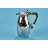 A GEORGE V SILVER ARTS AND CRAFTS INFLUENCE HOT WATER JUG, spot hammered with tendril thumb piece,