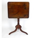 An early 19thC mahogany table with a rectangular tilt top above a turned pedestal base and three