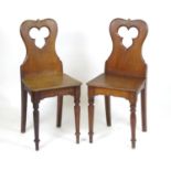 A pair of Victorian hall chairs with shaped back rests, pierced trefoil decoration and raised on