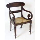 A Regency mahogany caned seated carver chair, having a large curved top rail above a caned seat,