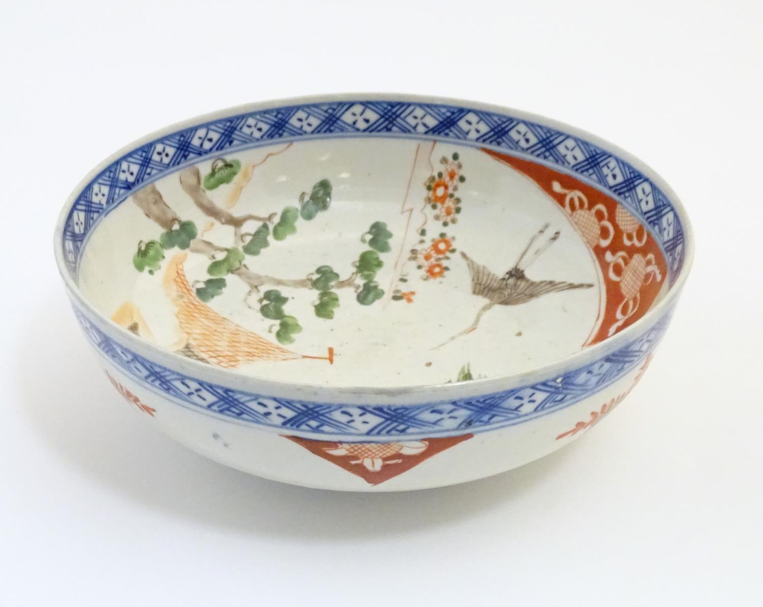 A Japanese bowl with hand painted decoration depicting a landscape scene with flowers, a crane