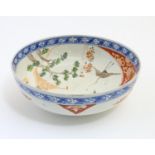 A Japanese bowl with hand painted decoration depicting a landscape scene with flowers, a crane