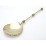 An unusual silver gilt serving spoon, the bowl having rounded serrated edge, the stem and terminal
