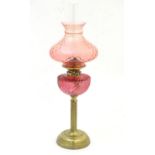 A Victorian oil lamp, the brass column with cranberry glass reservoir and shade. The twin burners