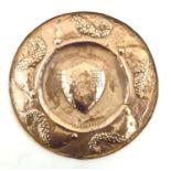 An Arts & Crafts Newlyn School style copper charger with embossed central shield with castle and