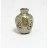 A Japanese silver plate ojime bead formed as a stylised vase with impressed detail and applied brass