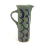 A studio pottery jug of cylindrical form with a green ground and blue detail. Impressed maker's mark