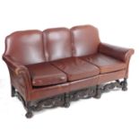 An early 20thC three seat leather sofa with scrolled arms and carved legs united by shaped